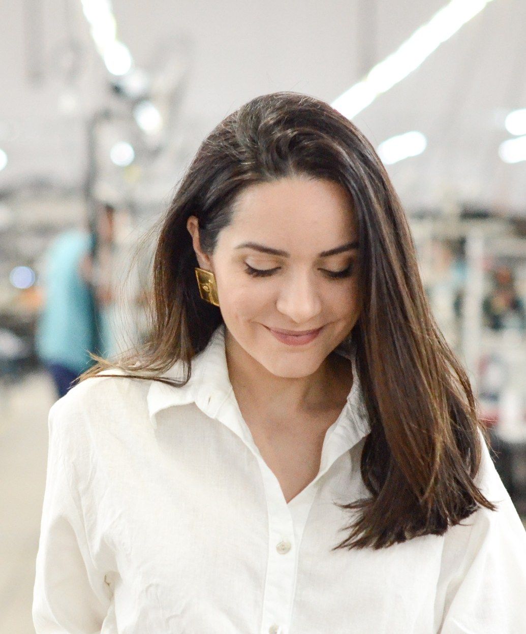 Erika Furtado sorrindo, de camisa branca de linho e calça cru, caminhando pelo salão de costura de uma fábrica